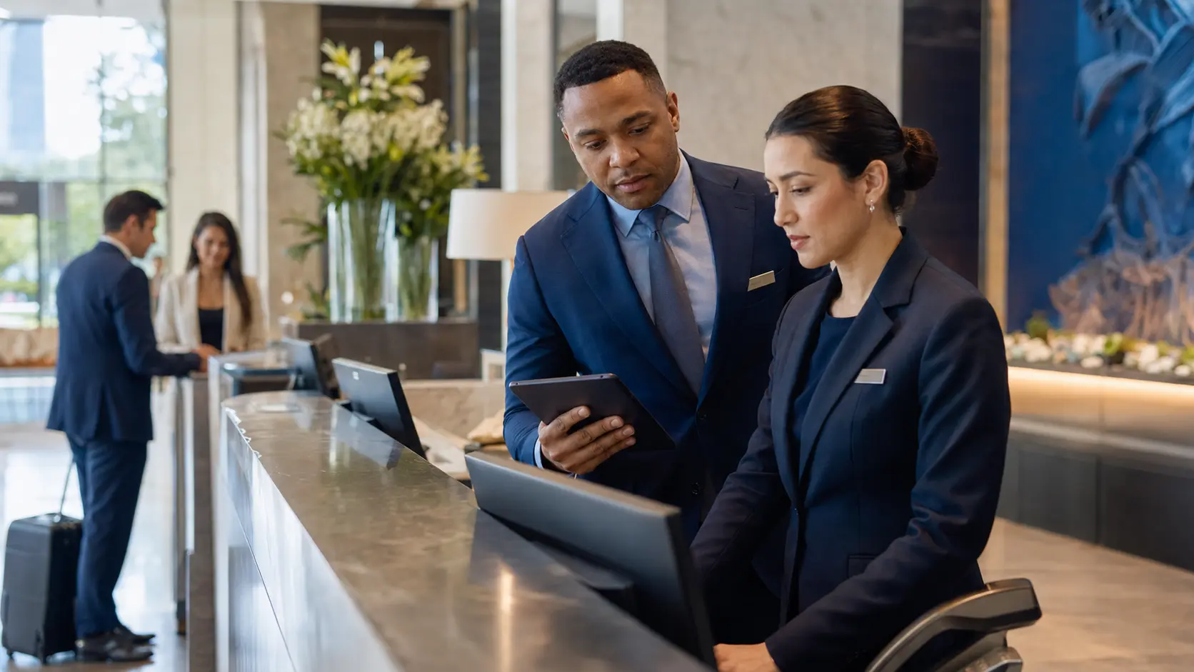A hotel front-office manager and front desk agent completing a practical shift-readiness check together at the reception desk.